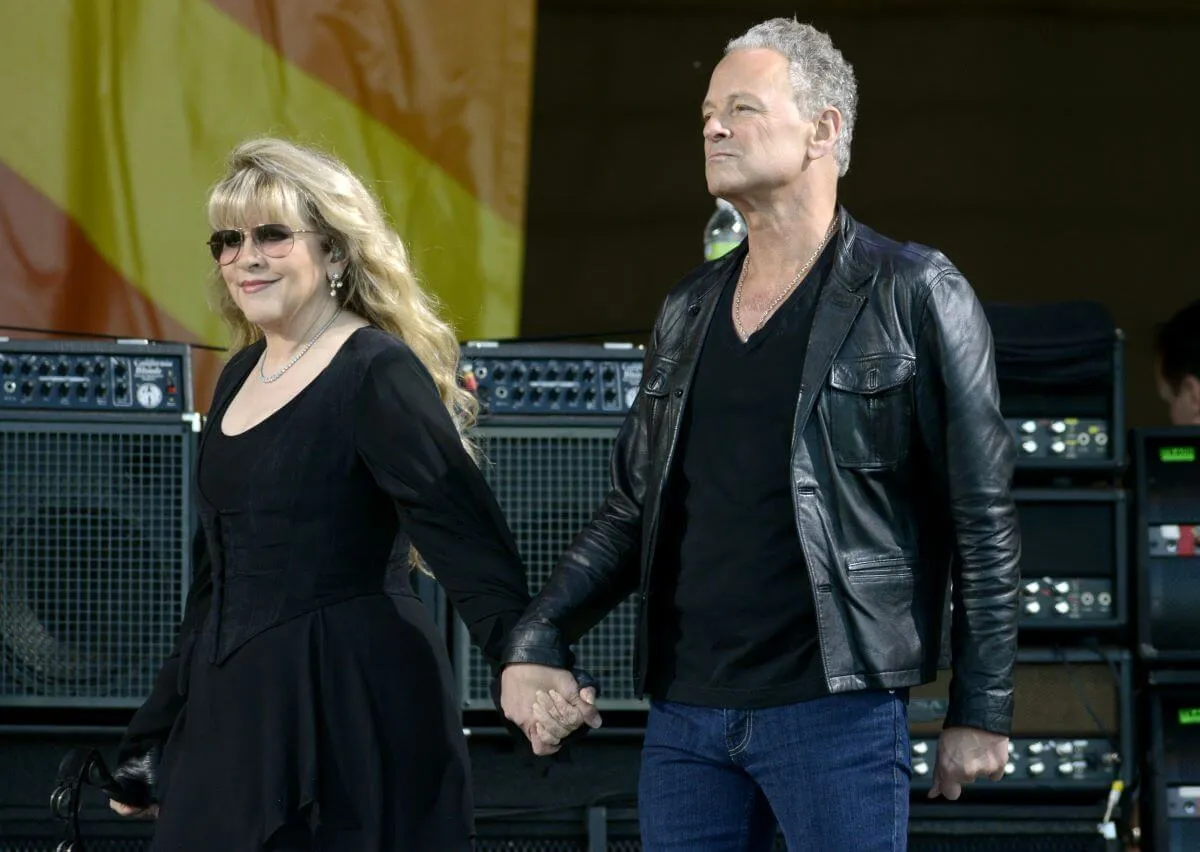 Stevie Nicks et Lindsey Buckingham portent toutes deux du noir et se tiennent la main sur scène lors d'un concert de Fleetwood Mac.