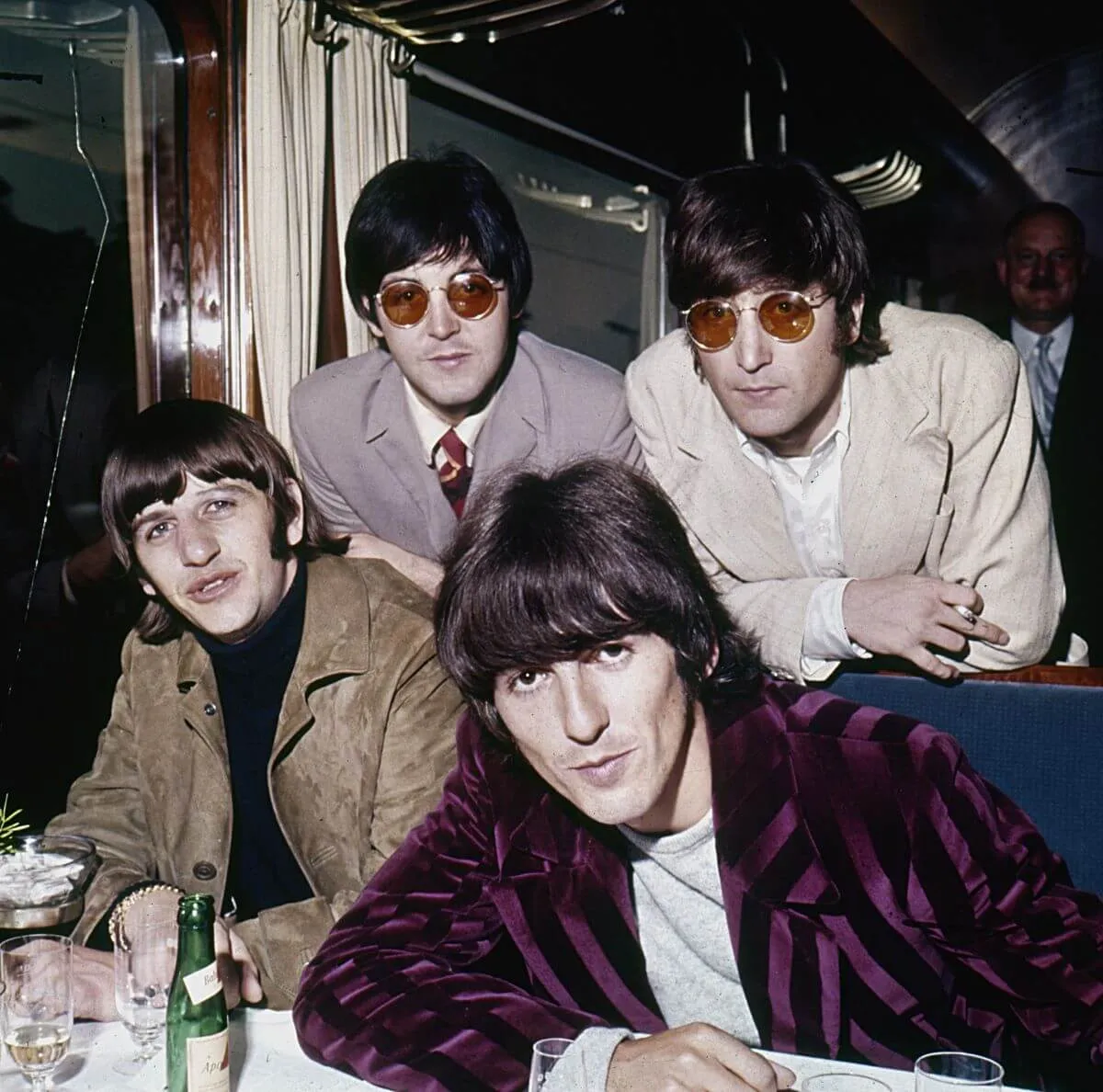 George Harrison, Ringo Starr, Paul McCartney et John Lennon se penchent sur une table.  McCartney et Lennon portent des lunettes circulaires teintées de rouge.