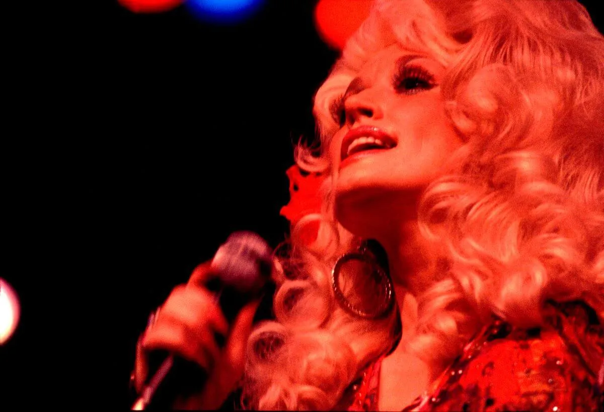 Dolly Parton chante dans un micro. Elle est éclairée par une lumière rouge.