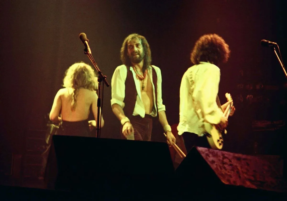 Mick Fleetwood se situe entre Stevie Nicks et Lindsey Buckingham.  Nicks et Buckingham ont le dos tourné et jouent de la guitare.