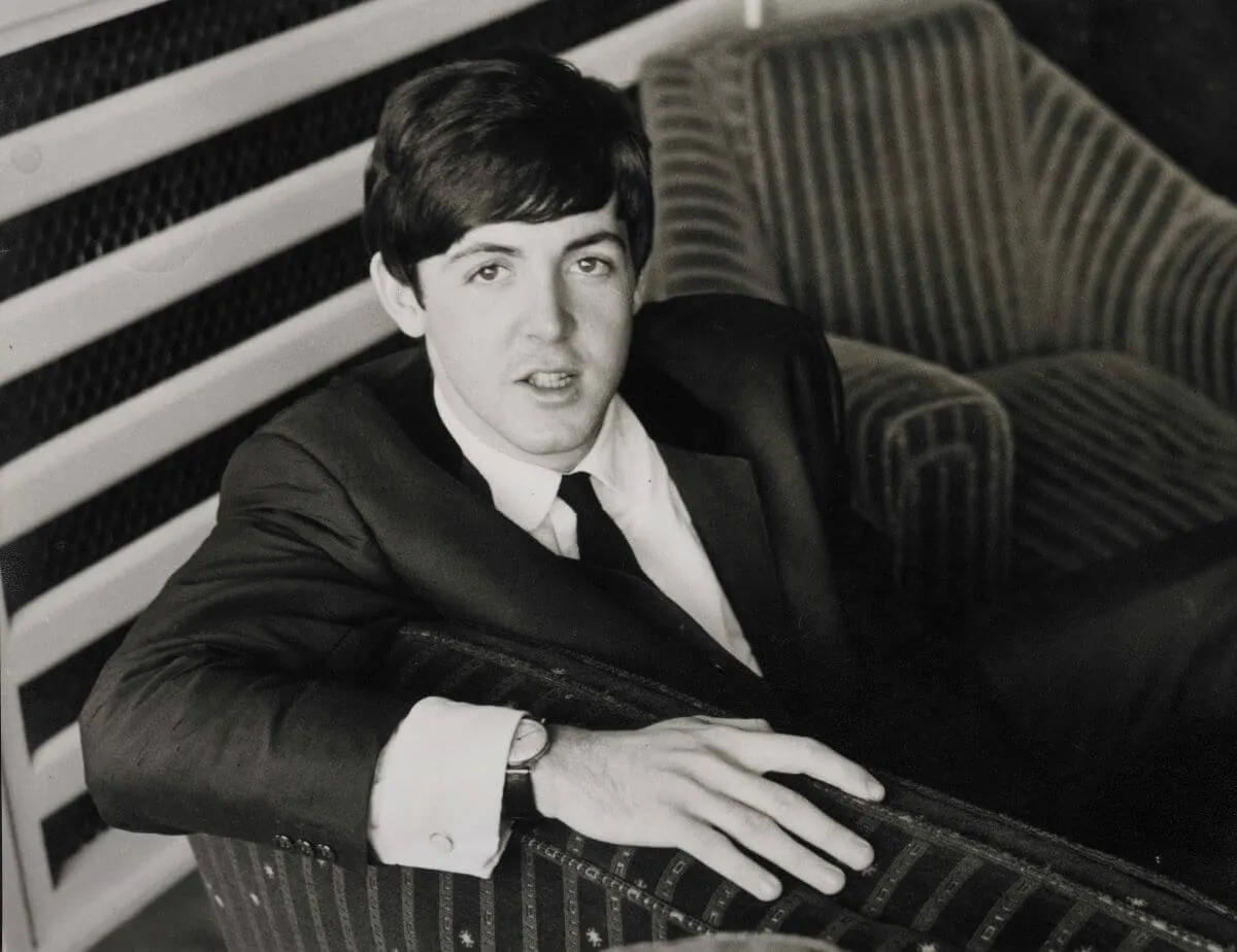 Une photo en noir et blanc de Paul McCartney portant un costume et assis sur une chaise.