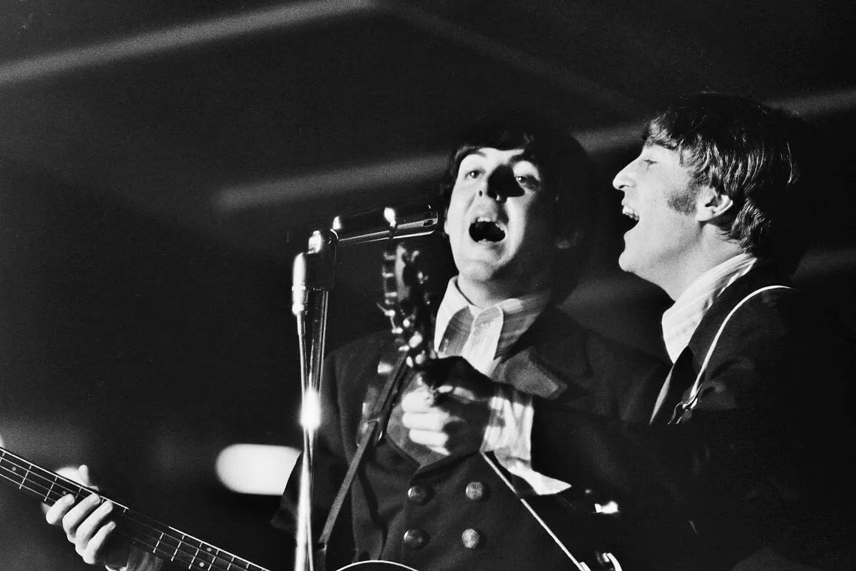 Une photo en noir et blanc de Paul McCartney et John Lennon chantant dans un microphone.