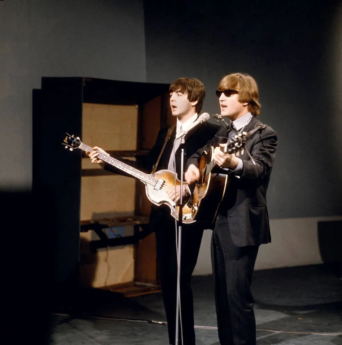 Paul McCartney et John Lennon portent des costumes et jouent de la guitare. Lennon porte des lunettes de soleil. Ils partagent un micro.