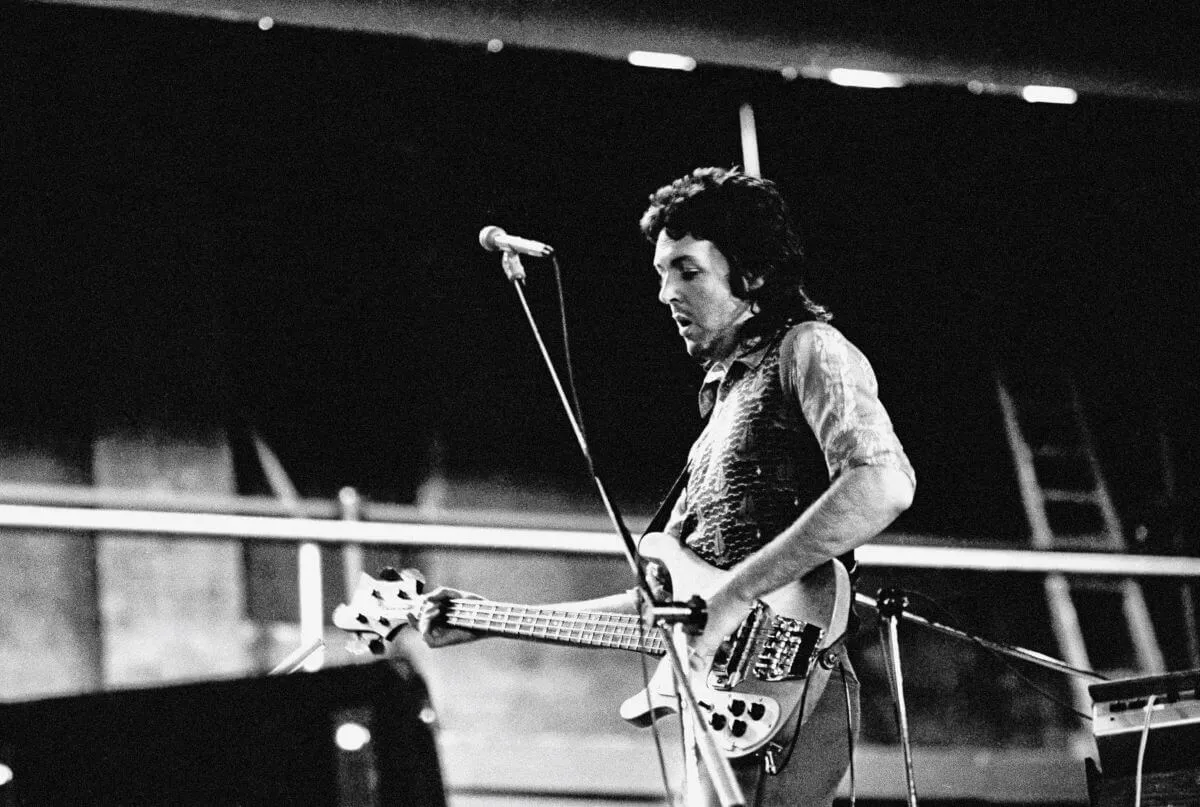 Une photo en noir et blanc de Paul McCartney tenant une guitare et debout derrière un microphone.