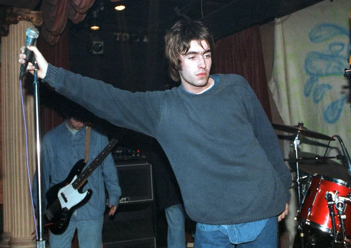 Liam Gallagher porte un pull et tient un microphone sur le côté.