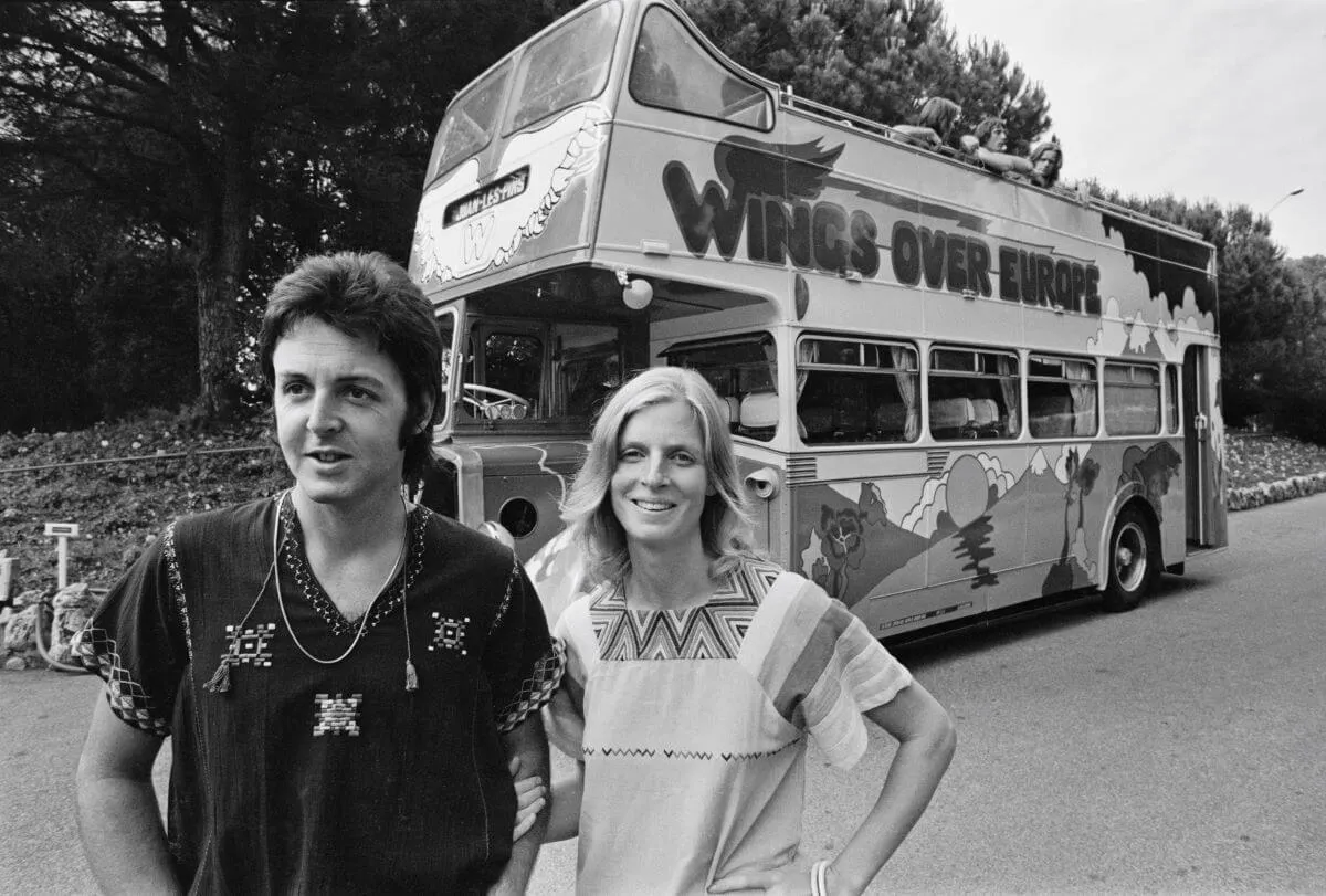Une photo en noir et blanc de Paul et Linda McCartney debout devant le bus de tournée Wings.