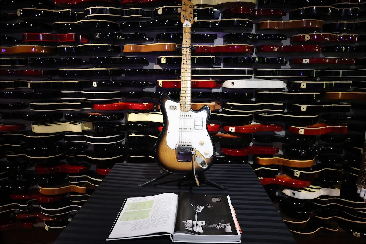 La guitare Futurama de George Harrison exposée devant un mur d'autres guitares horizontales