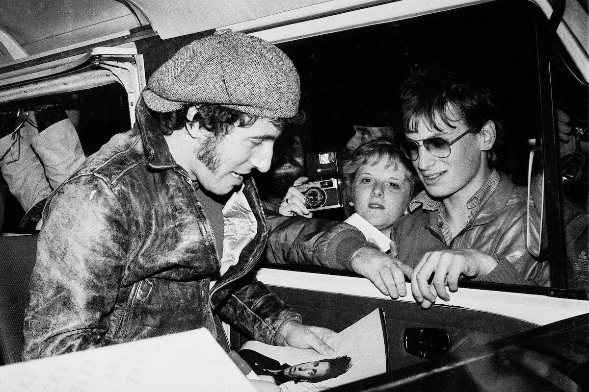 Photo en noir et blanc de Bruce Springsteen dans une voiture en train de signer un autographe pour un fan