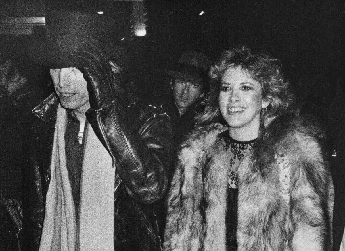 Une photo en noir et blanc de Tom Petty portant un haut-de-forme et marchant avec Stevie Nicks. Elle porte un manteau de fourrure.