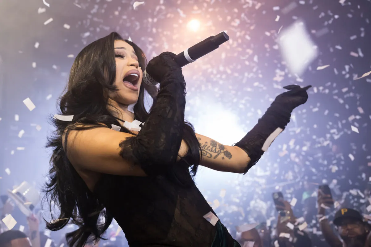 Cardi B porte des gants noirs jusqu'aux coudes et tient un microphone.