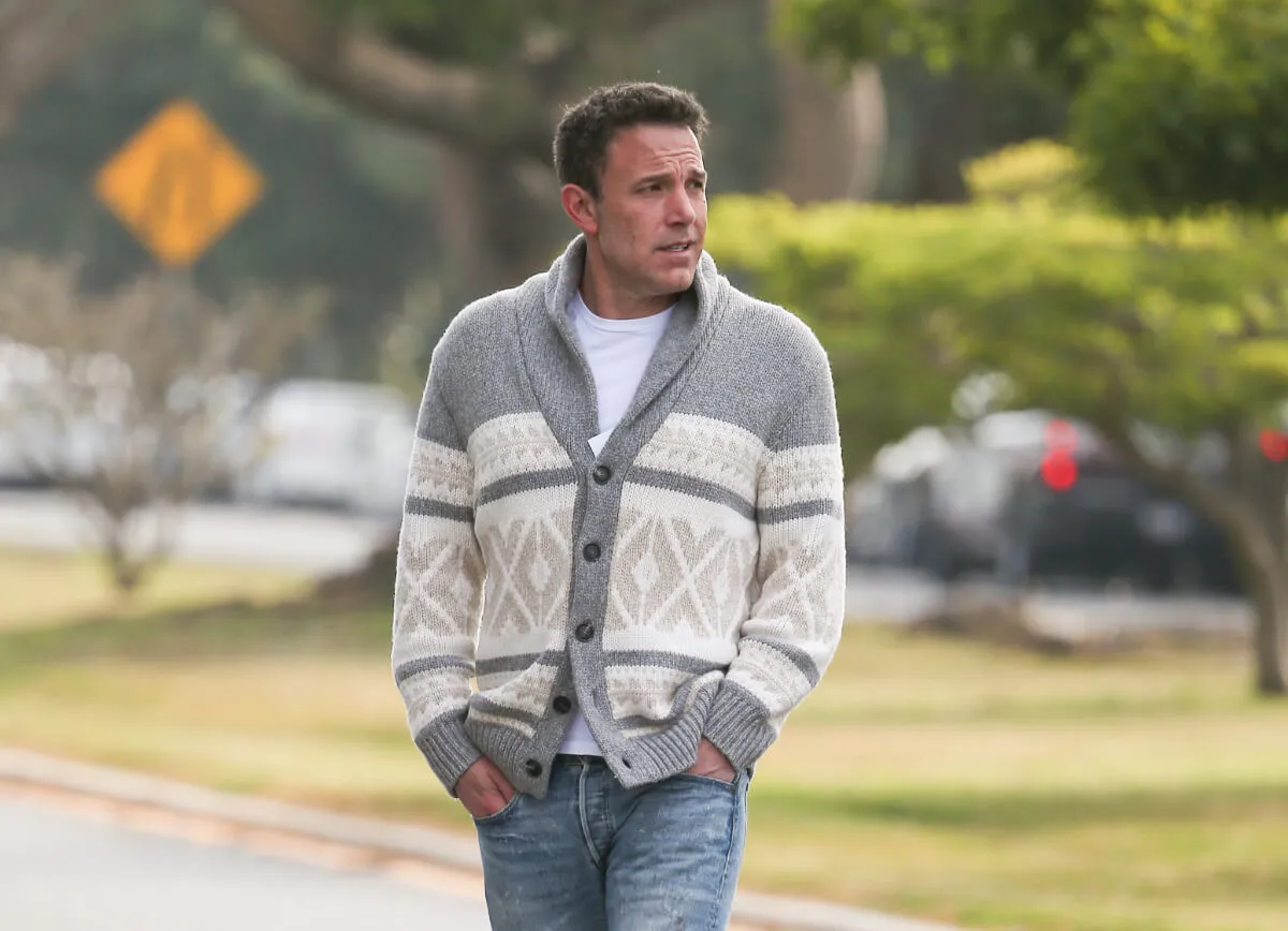 Ben Affleck porte un pull blanc et gris et sort les mains dans les poches.