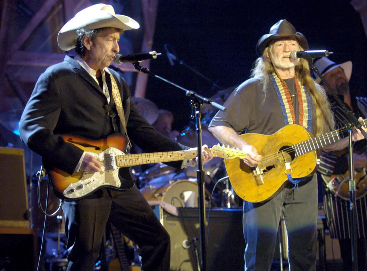 Bob Dylan et Willie Nelson jouent de la guitare et se tiennent devant des microphones.