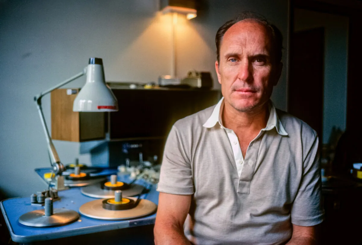 Robert Duvall porte un polo gris et est assis devant une table avec un film.