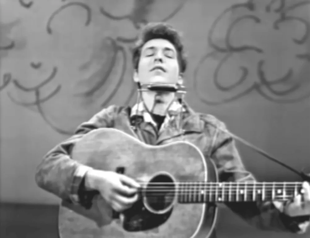 Capture d'écran en noir et blanc de Bob Dylan jouant de la guitare à la télévision en 1963.