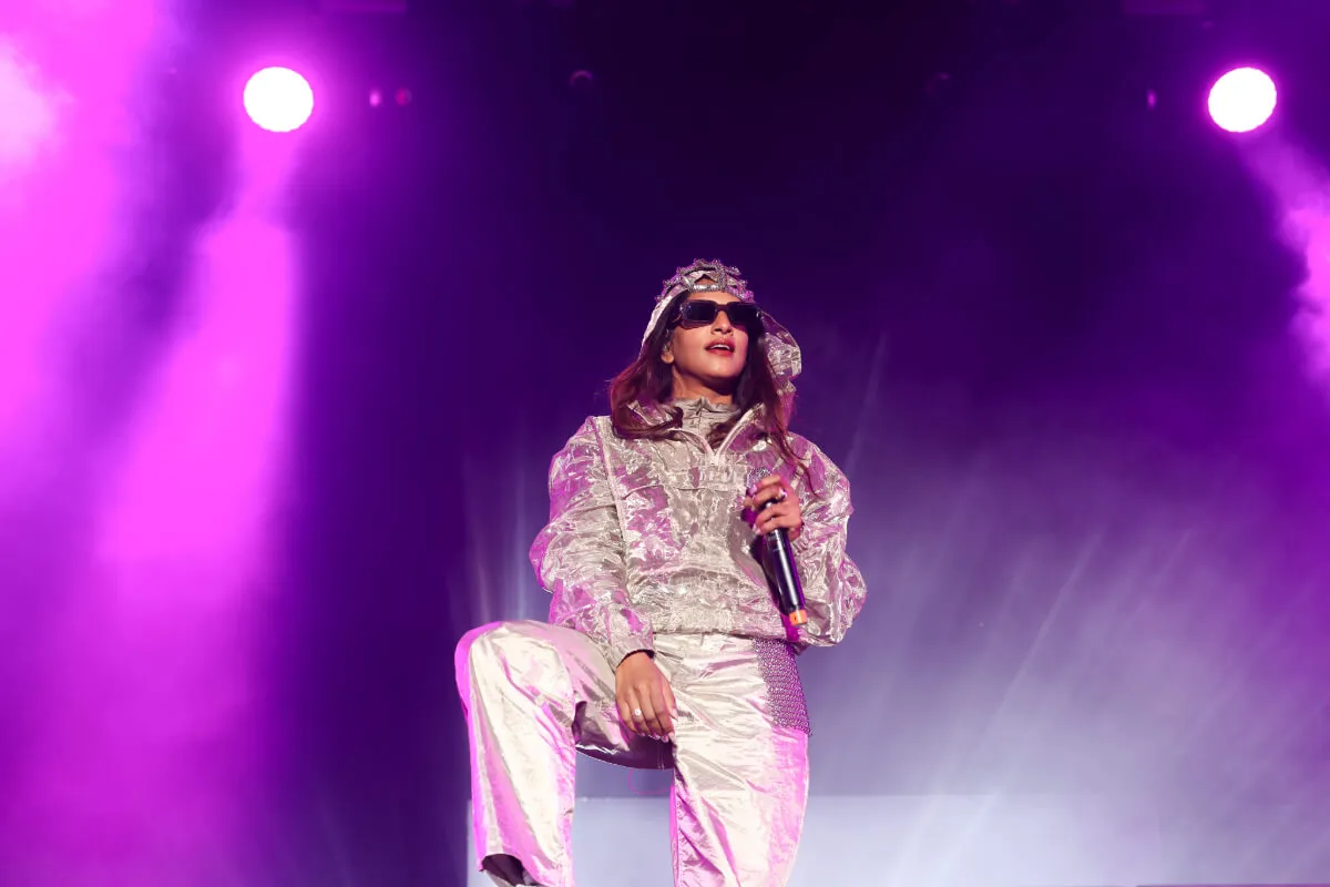MIA porte de l'argent et des lunettes de soleil et se tient debout avec un microphone.